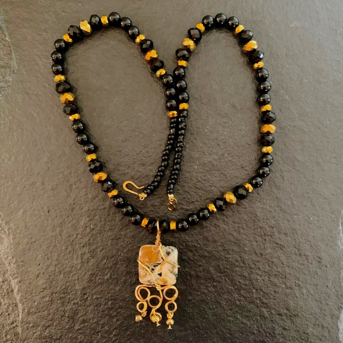 A necklace made of Black & Gold Square Jasper pendant with Onyx beads and gold crystals