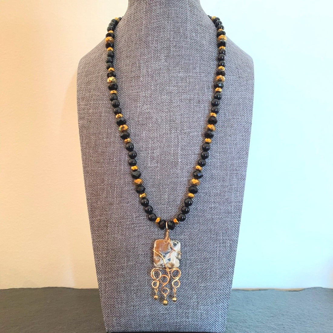 A necklace made of Black & Gold Square Jasper pendant with Onyx beads and gold crystals